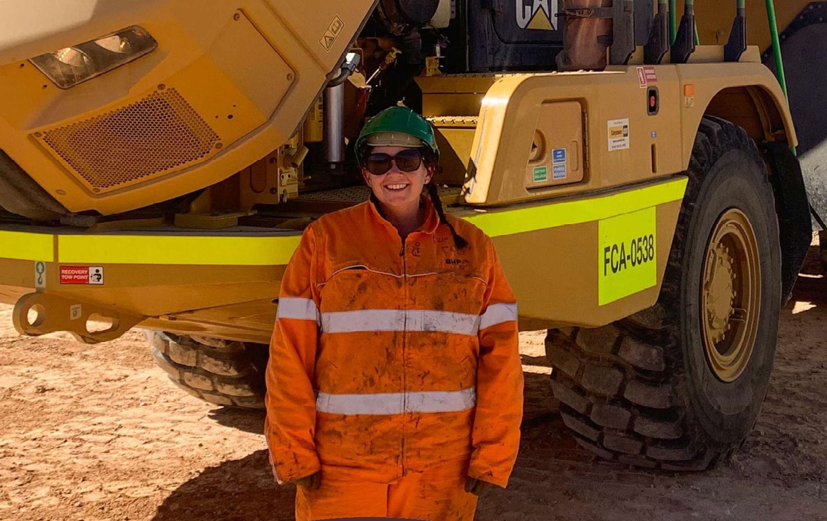 Team member in orange workwear standing in front of a haul truck
